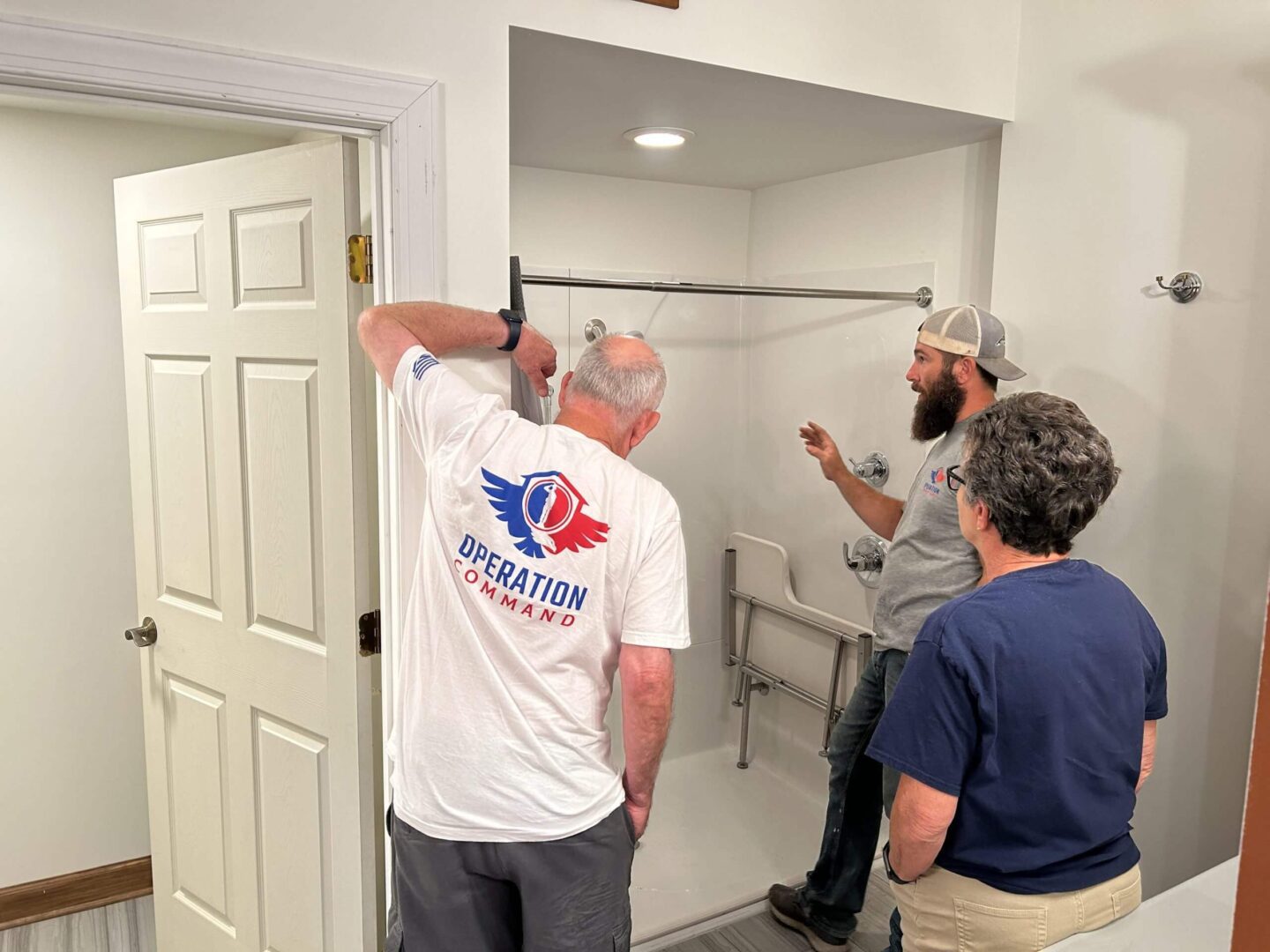 Three people installing or inspecting a shower door in a bathroom.