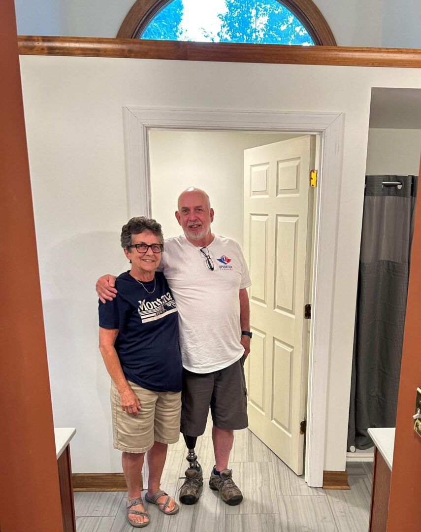 Two smiling men standing together in a hallway, one with a prosthetic leg.