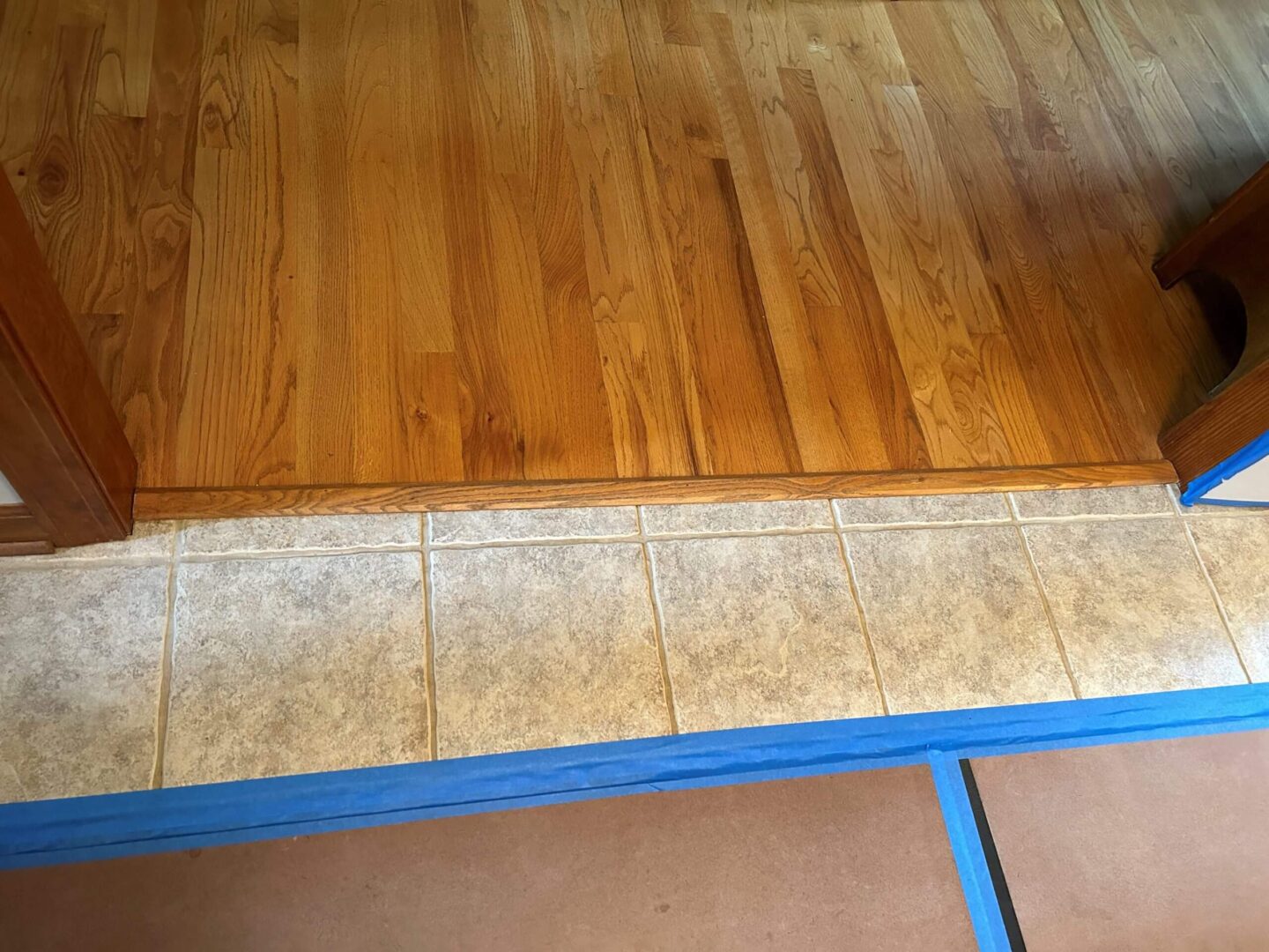 Transition between tiled floor and wooden flooring with blue painter's tape.
