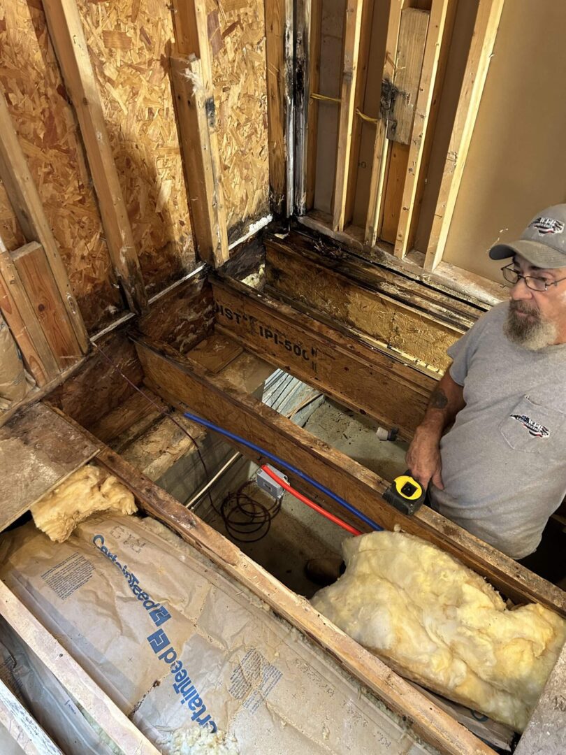 Man inspecting exposed wooden floor joists and insulation during home renovation.