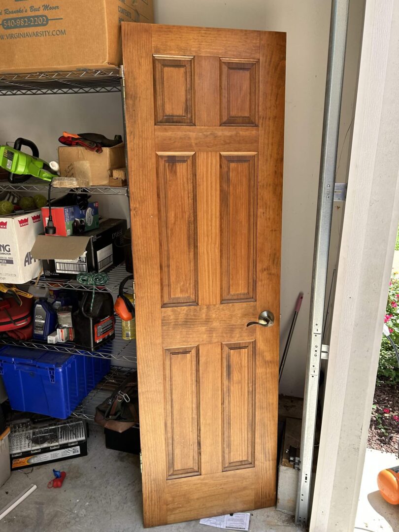 A wooden six-panel door leaning in a garage filled with tools and storage items.