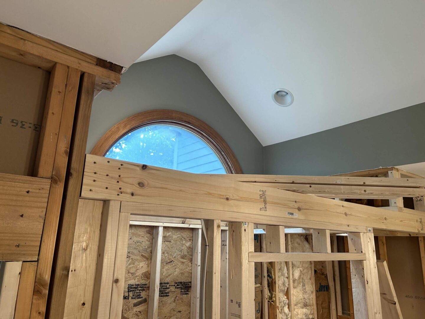 Interior view of wooden framing and a large arched window under construction.